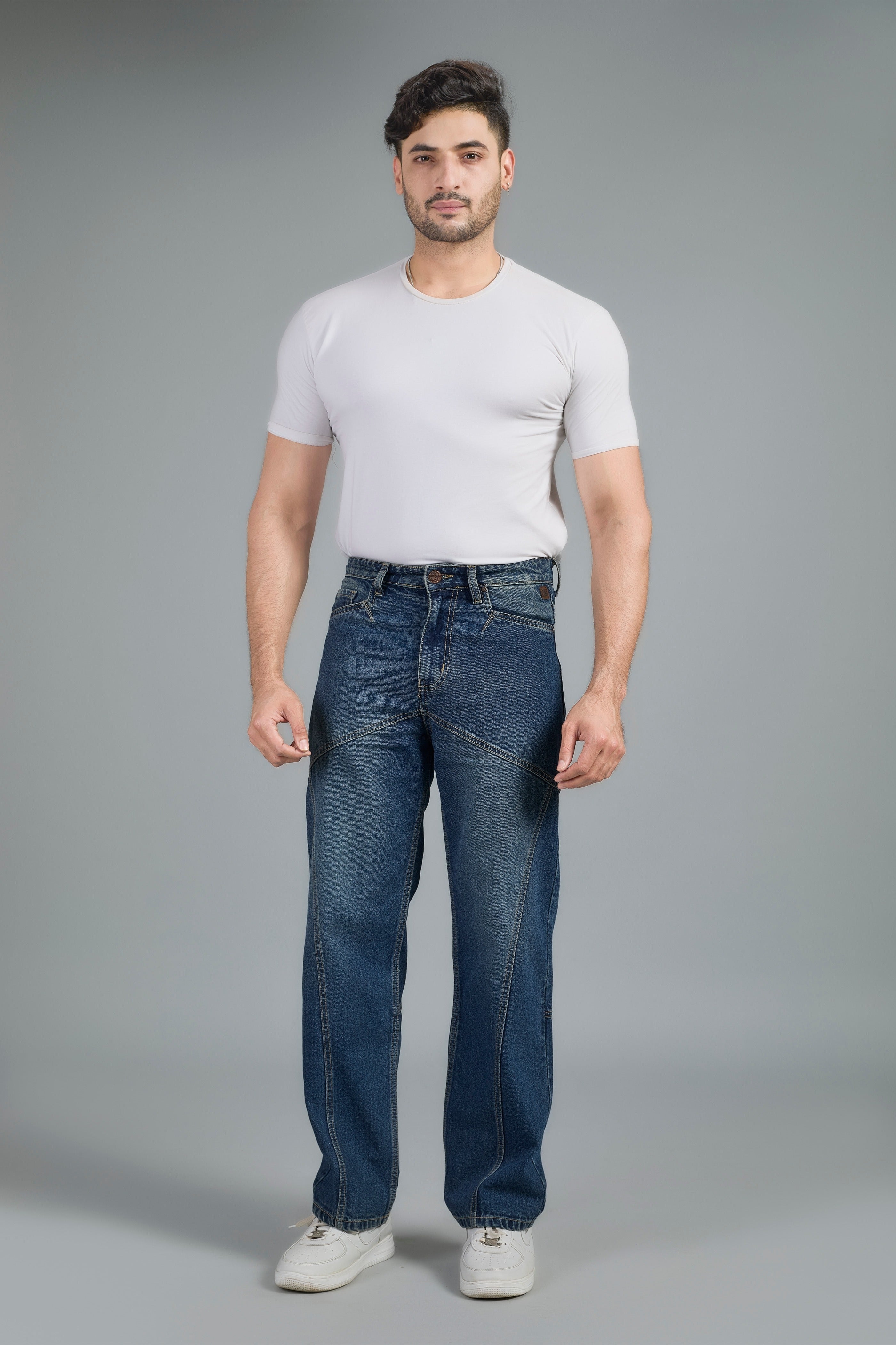 Man wearing a white t-shirt and blue jeans against a gray background