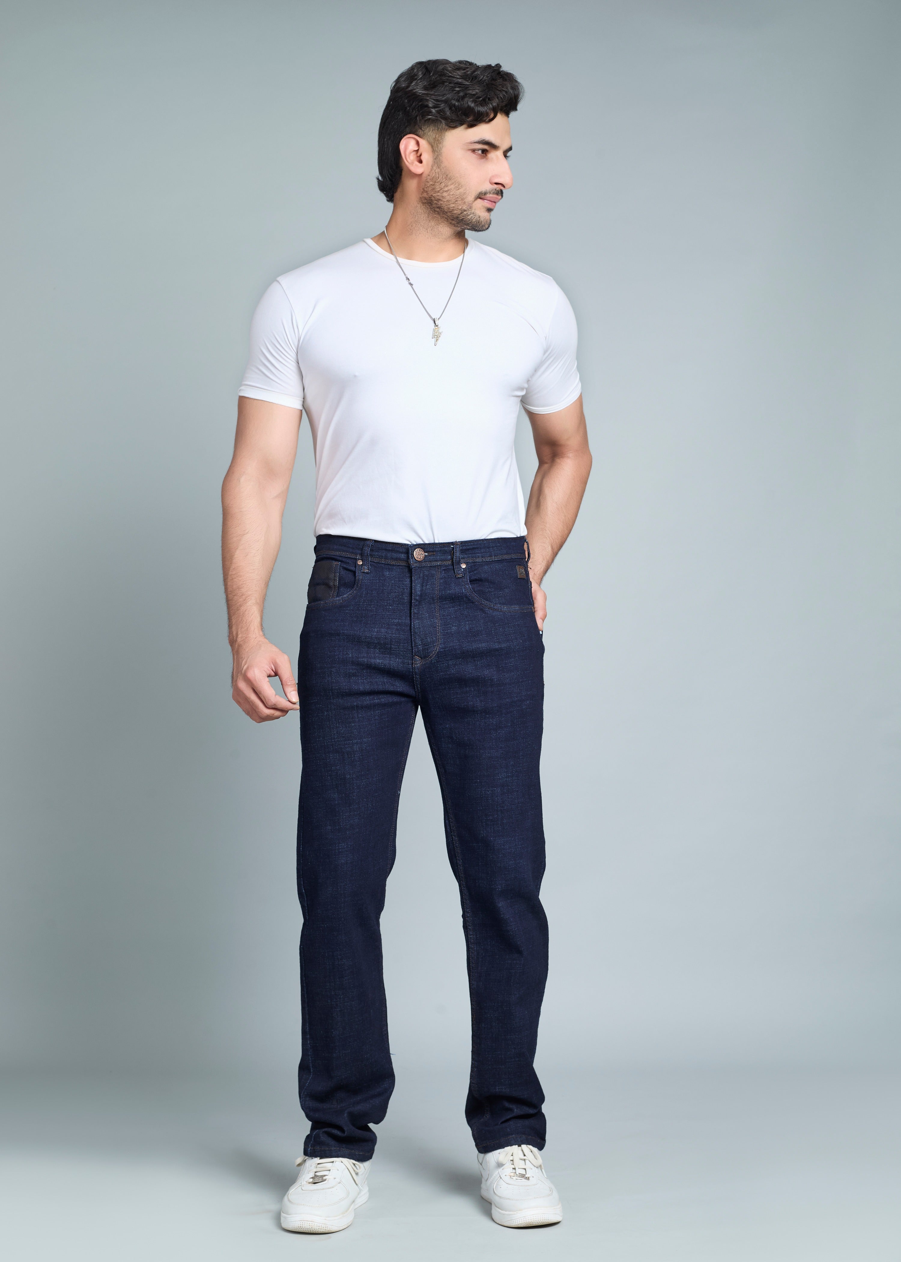Man wearing a white t-shirt and dark jeans against a gray background
