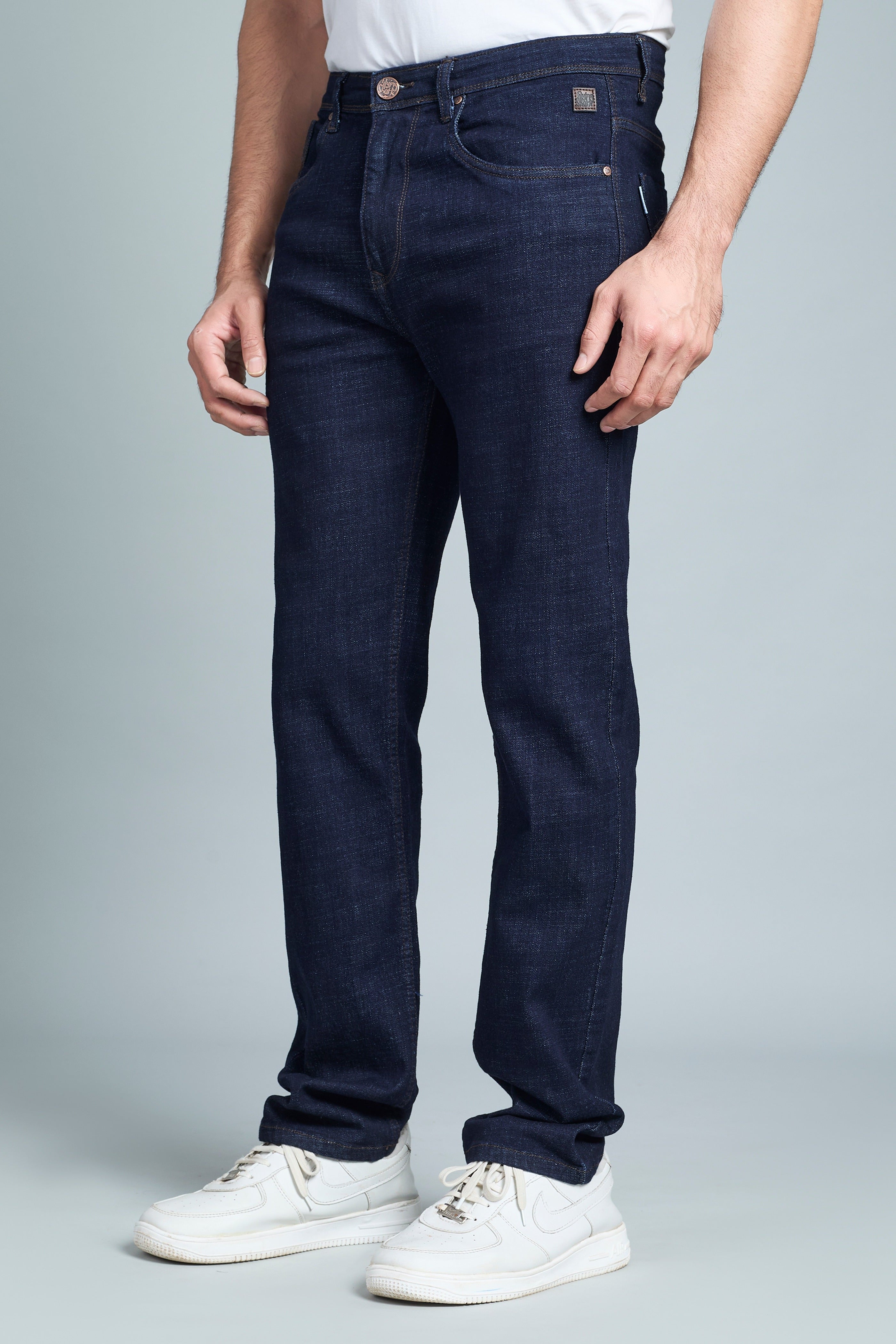 Person wearing dark blue jeans and white sneakers on a gray background