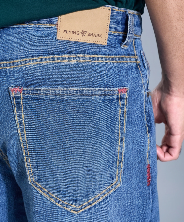 Close-up of blue jeans with a brand label on the back pocket against a neutral background